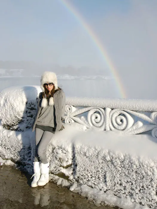 Woman in grey and white Sorel Boots sitting on edge of frozen niagara falls.