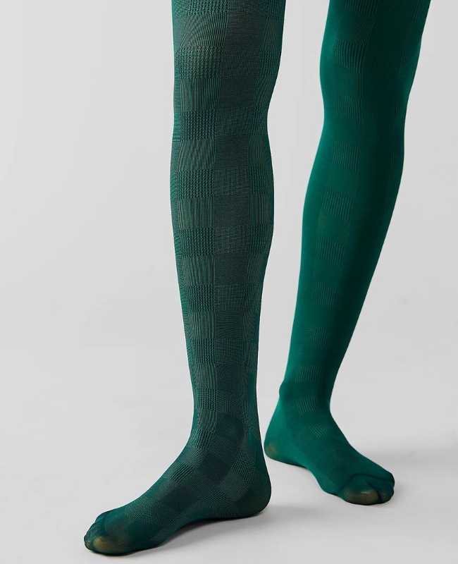 Close up of woman's legs wearing dark green opaque stockings on grey background.