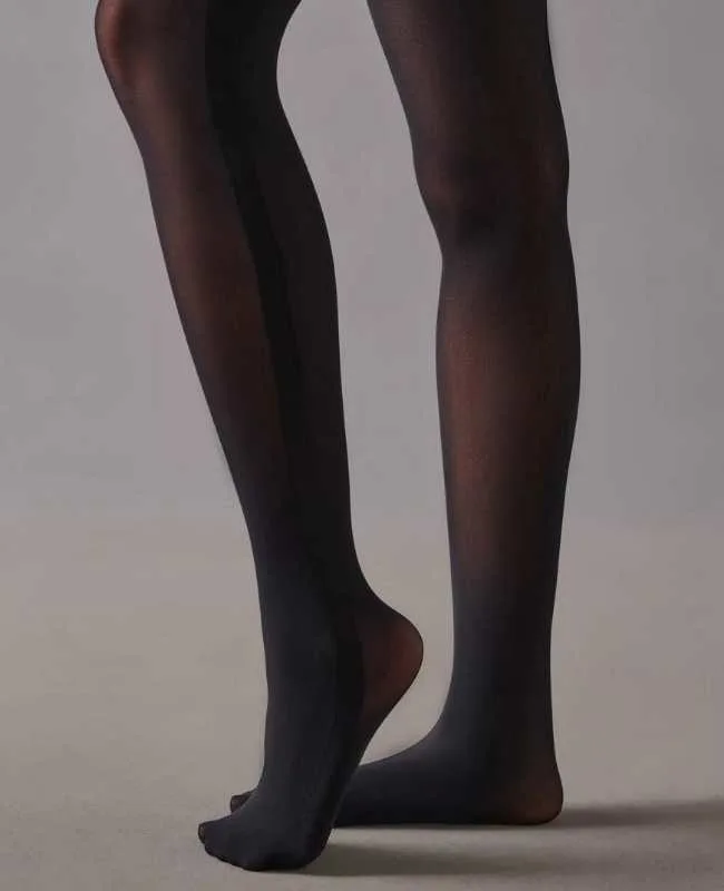 Close up of woman's legs wearing semi-sheer black stockings on grey background.