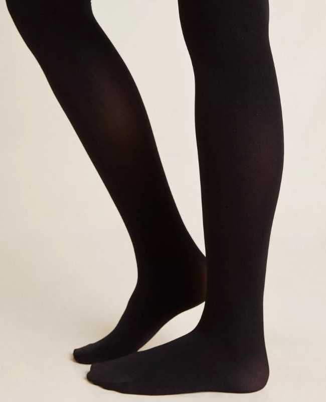 Close up of woman's legs wearing opaque black stockings on beige background.