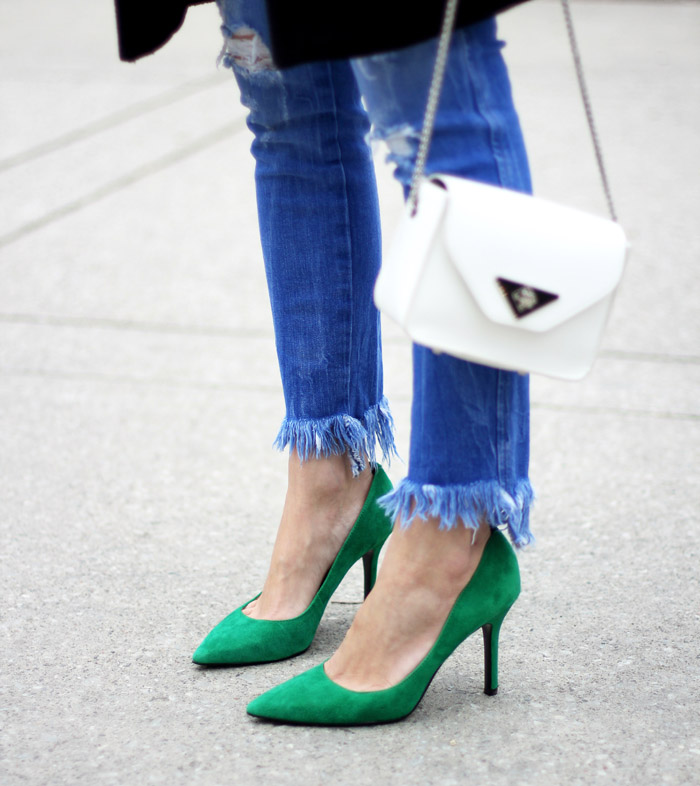 Close up of woman wearing a green shoes outfit with green heels, fringe denim blue jeans and white purse.