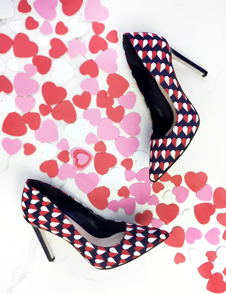 Printed heart shoes on a white floor sprinkled with red and pink hearts.