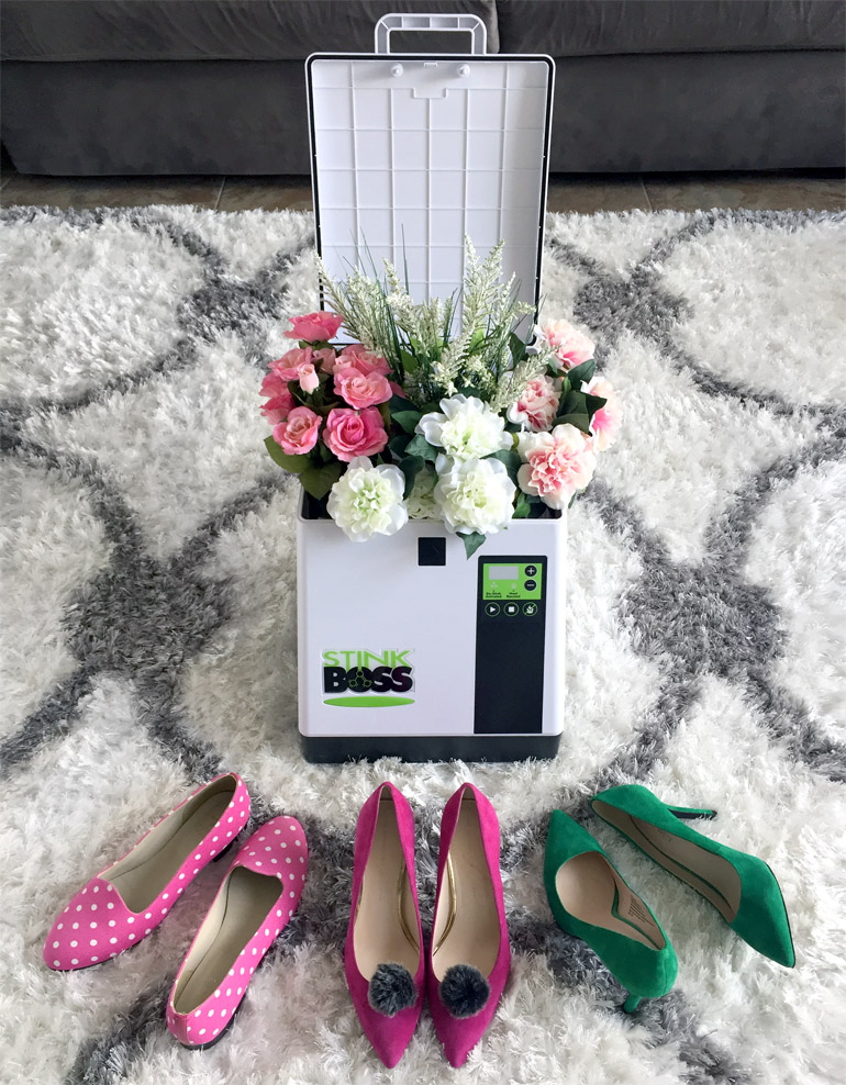 STinkboss shoe deodorizer machine with flowers inside and pink and green shoes surrounding it on a carpet.