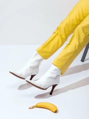 Image insinuating Slippery Shoes in post about how to make shoes less slippery with woman's legs wearing white boots and yellow pants near banana laying on ground.