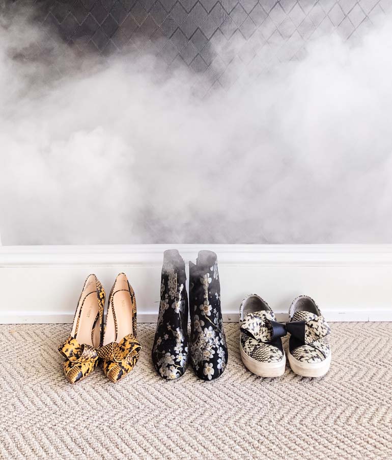3 pairs of stinky shoes lined up against a wall with smelly smoke around them.