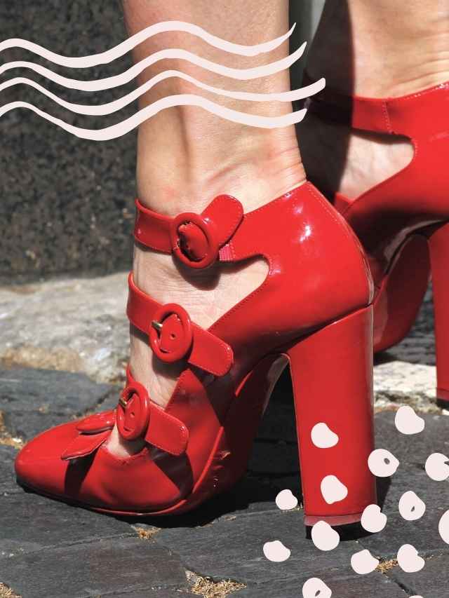 Close up of woman's feet wearing strappy red patent block heels pumps on concrete.
