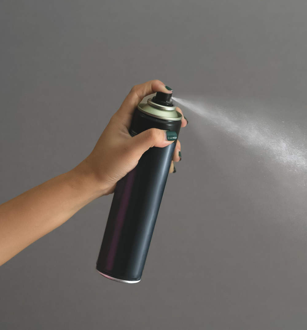 Close up or of woman's arm spraying hairspray on a grey background.