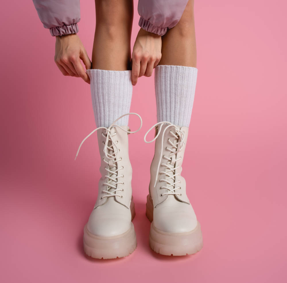 Woman pulling up white socks and wearing blush pink combat boots.