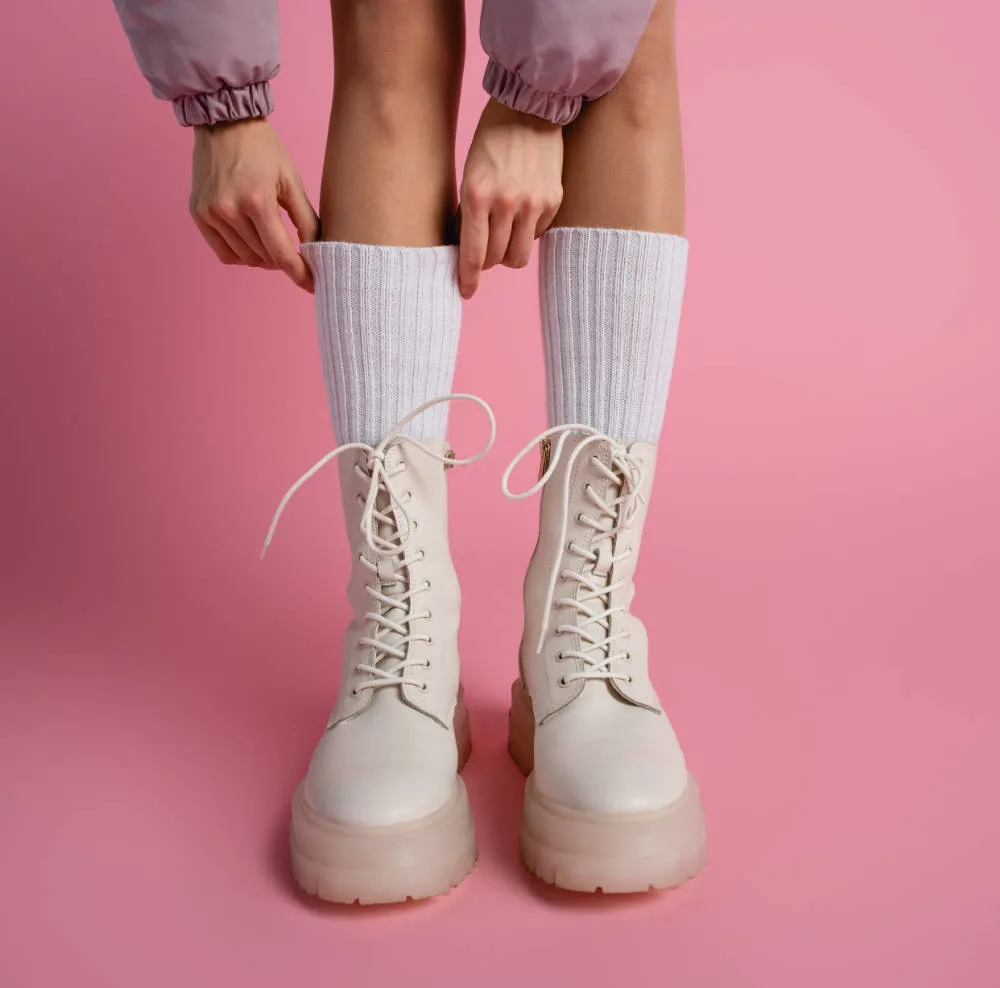 Woman pulling up white socks and wearing blush pink combat boots.