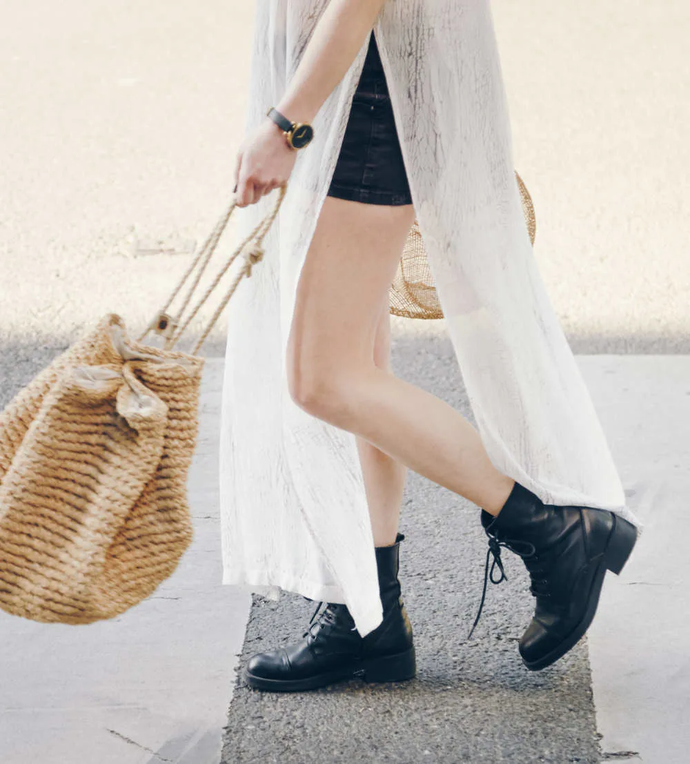 Woman walking wearing combat boots with mini skirt, long tunic and straw bag.