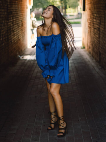 Woman wearing black shoes with blue dress standing under a bridge.