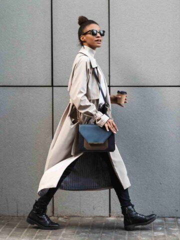 Woman walking wearing combat boots, trench coat and purse.