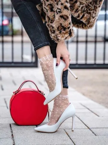 Close up of woman wearing white heels trying to keep heels from slipping out of shoes.