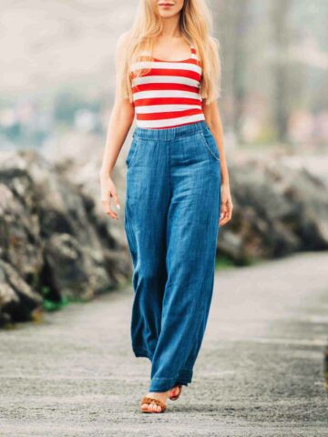 Blonde woman wearing sandal shoes with wide leg jeans with red and white tank top as she is walking outside.