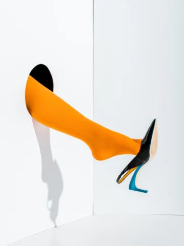 Woman's leg coming out of hole in the wall wearing orange stocking and black slingback heel.