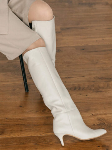 Cropped view of woman wearing white kitten heel knee boots.
