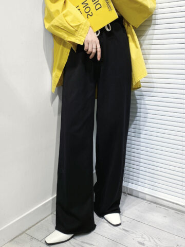 Cropped view of woman wearing white shoes with wide leg pants and yellow jacket.