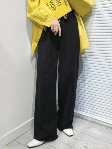 Cropped view of woman wearing white shoes with wide leg pants and yellow jacket.