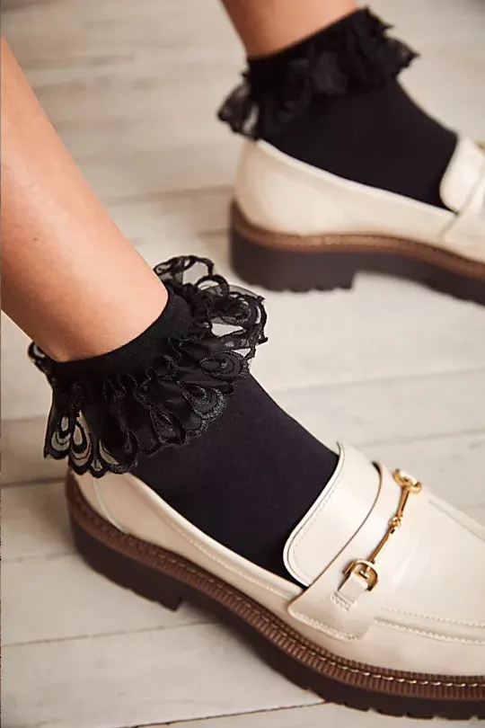 Close up of woman's feet wearing black lace frill ankle socks with white loafers.