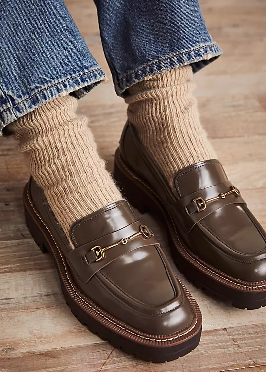 Close up of woman's feet wearing beige wooly socks with khaki loafers and straight leg blue jeans.