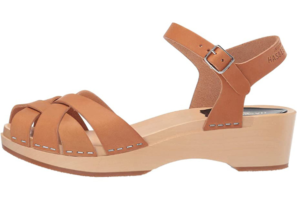 Clog style sandals in tan leather on light wooden shoe resting on white background.