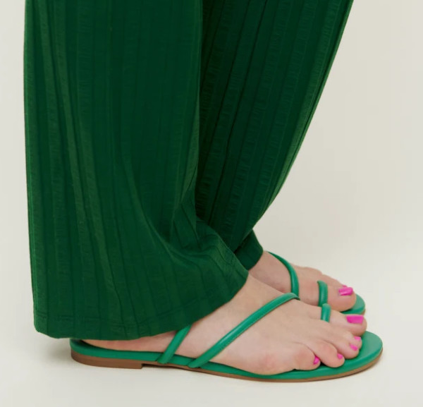 Cropped view of woman wearing green toe loop sandals long baggy dark green pants with hot pink nail polish.