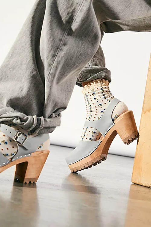 Cropped view of woman wearing light blue sandal clogs with socks and cuffed grey jeans.