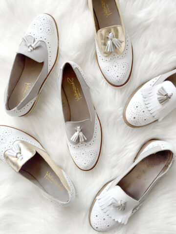 Multiple white and gold loafers on a furry white carpet.