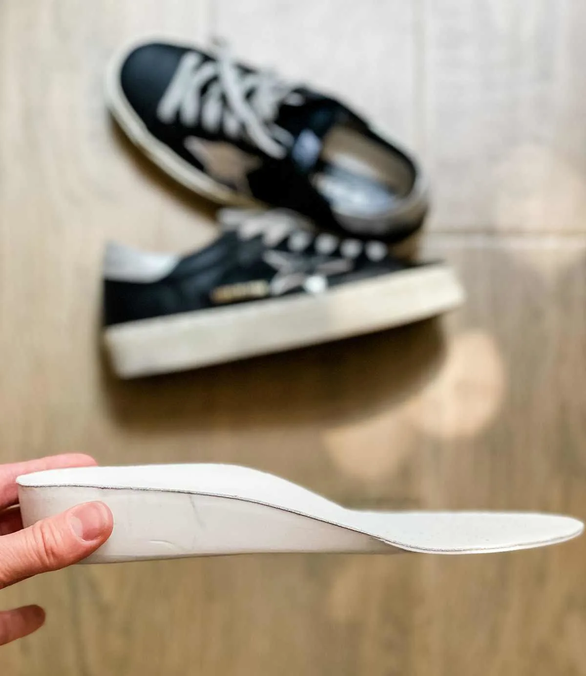 Woman holding a wedge insole over a pair of black Golden goose Hi star sneakers.