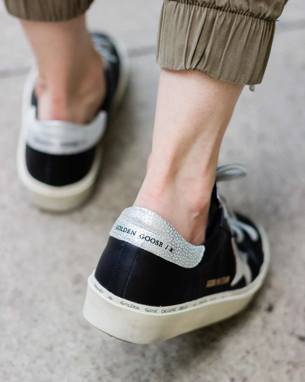 Back close up view of woman wearing black golden goose hi star sneakers while walking on concrete sidewalk.