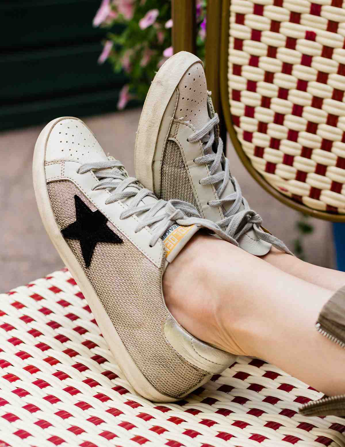 Close up of woman's feet wearing off-white golden goose star sneakers on a woven chair.