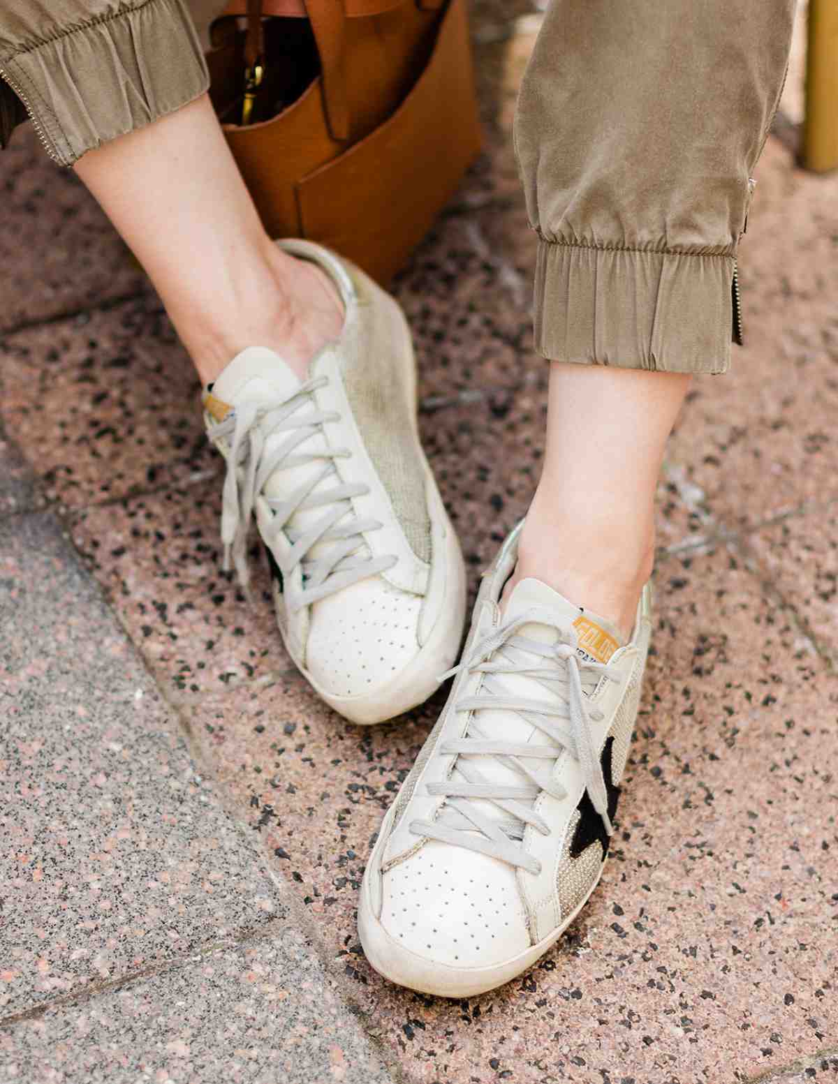 Top view of woman's feet wearing off-white golden goose superstar sneakers with khaki pants on a pink speckled concrete.