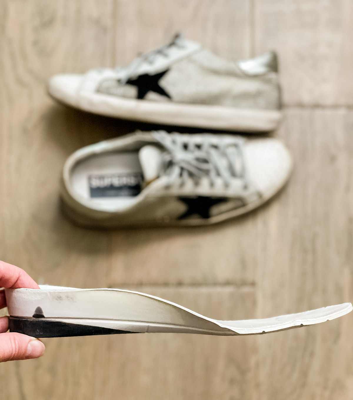 Woman holding a wedge insole over a pair of off-white Golden goose superstar sneakers.