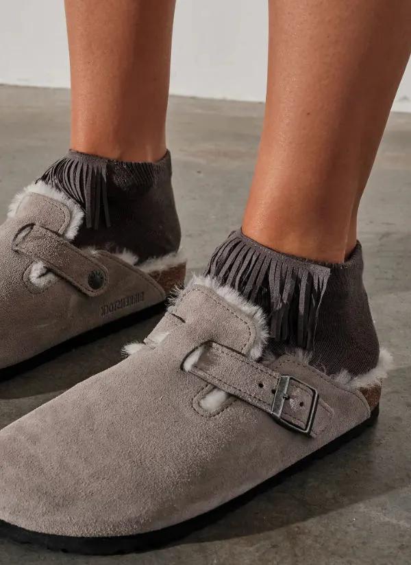 Close up of woman's feet wearing Grey shearling lined Birkenstock clogs with fringe socks.