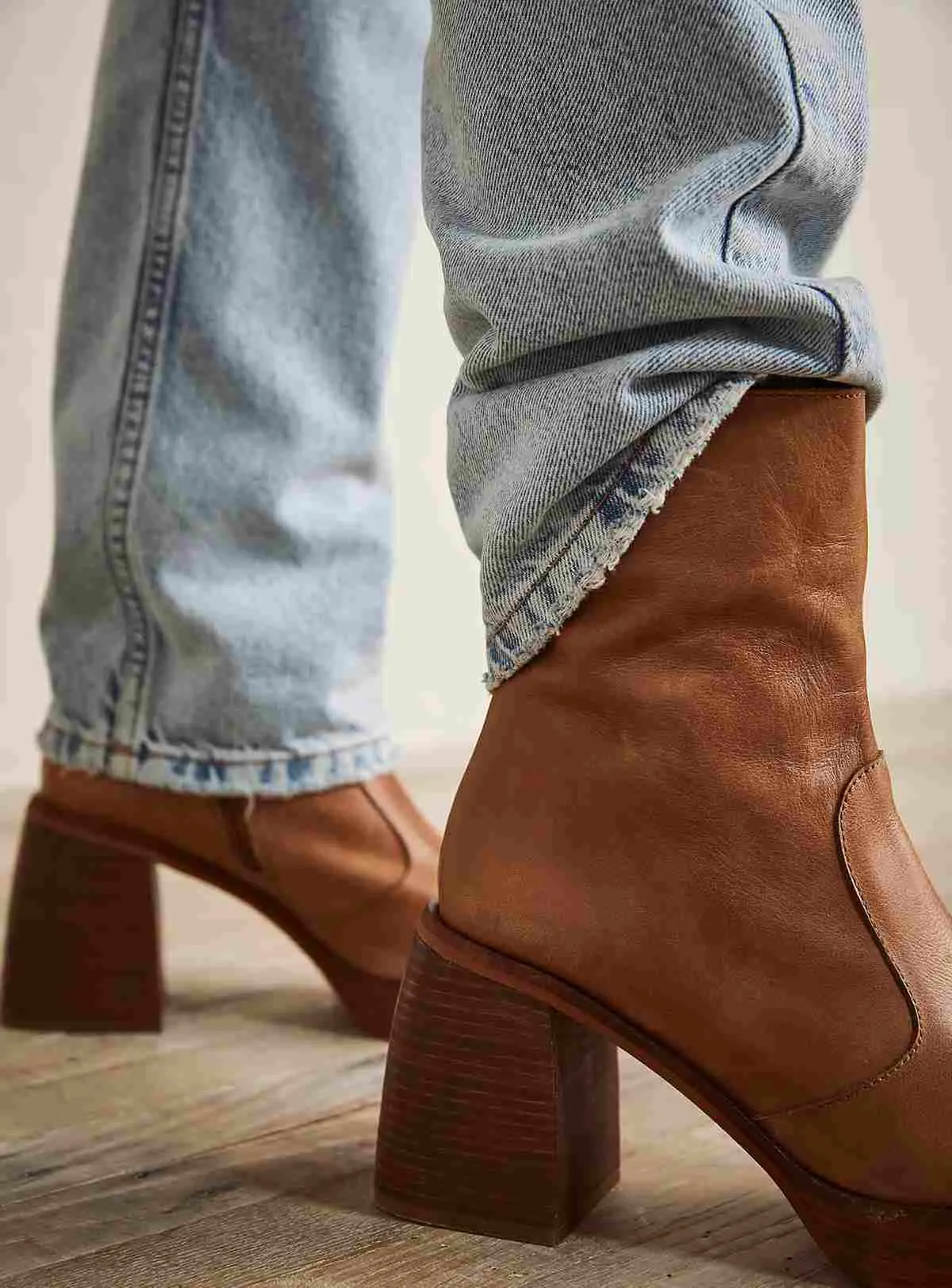 Close up of women's feet wearing chunky heel brown ankle boots with light wash jeans, one pant leg half tucked into boot.