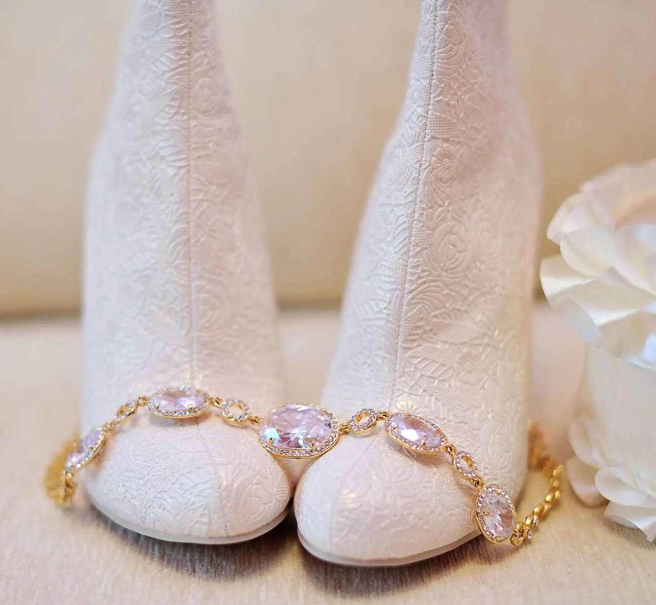 White brocade wedding ankle boots on table with necklace laid on top.