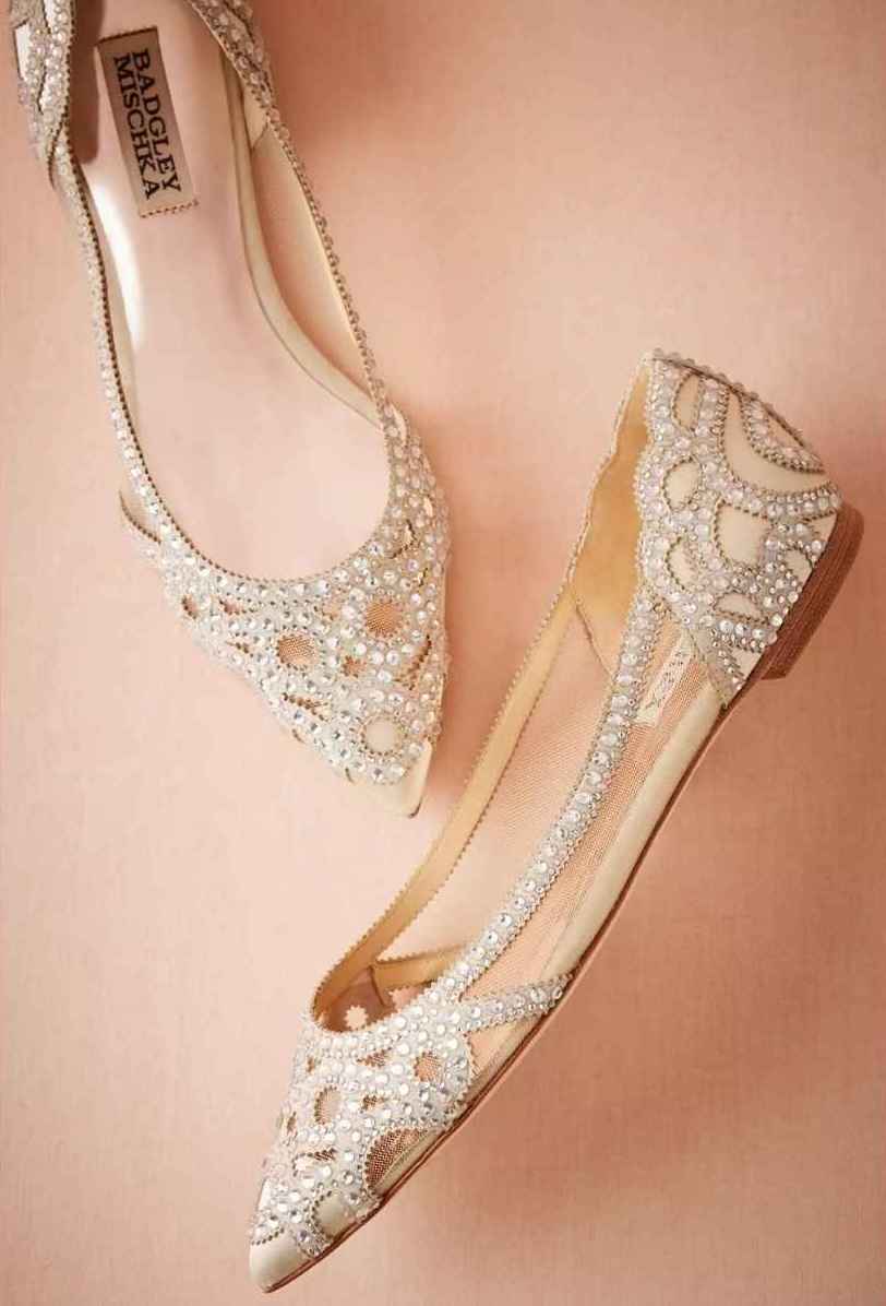 Pair of bejewelled white and clear pointed toe wedding flats on pink background.