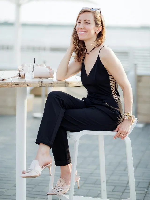 Lady sitting on patio, wearing pink slide shoes with a black jumpsuit.