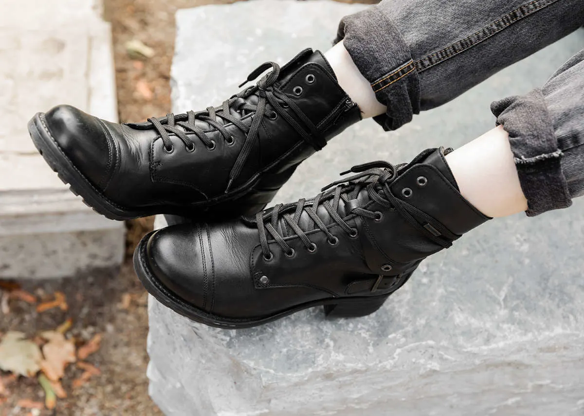 From above cropped view of woman's feet wearing Taos crave combat boots in black waterproof with cuffed grey jeans on a sidewalk.