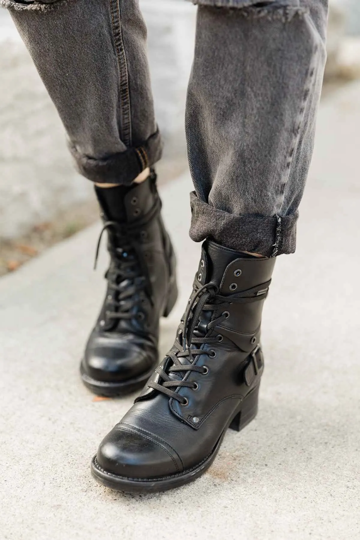 Front cropped view of woman's feet wearing Taos crave combat boots in black waterproof with cuffed grey jeans on a sidewalk.