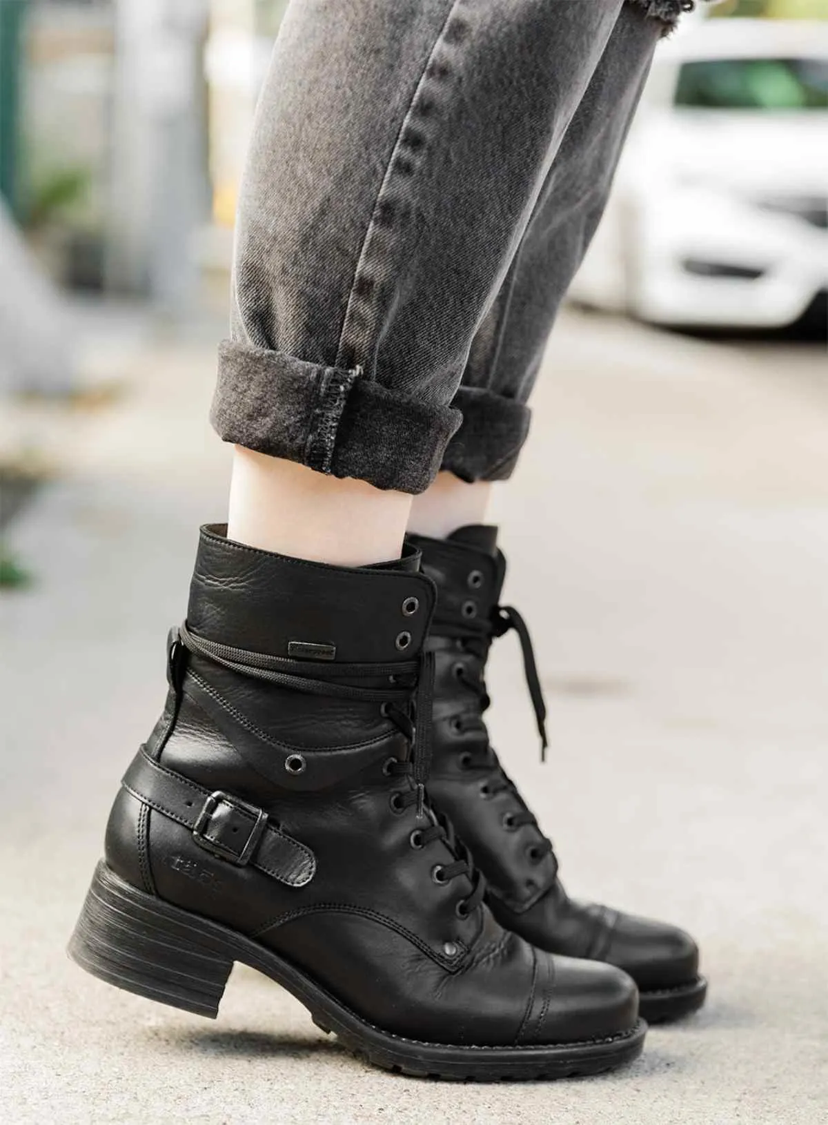 Cropped view of woman's feet wearing Taos crave combat boots in black waterproof with cuffed grey jeans on a sidewalk.