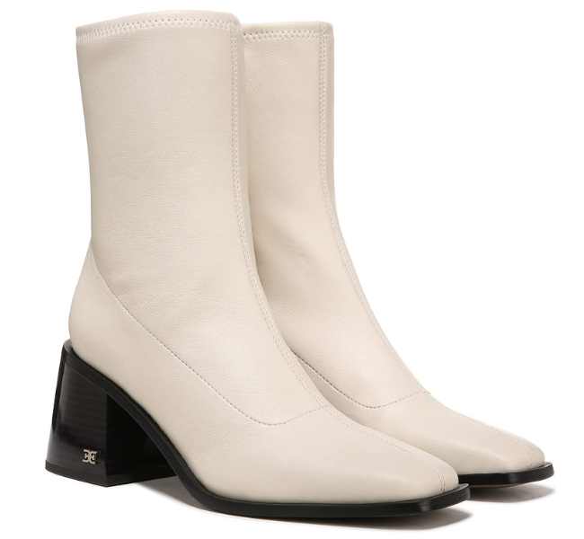 Pair of off white sock boots with black heels and square toe on white background.