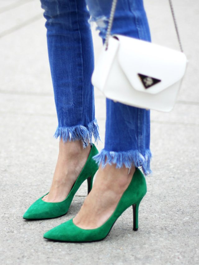 Close up image of women wearing jeans with a pair of green heels on grey background.