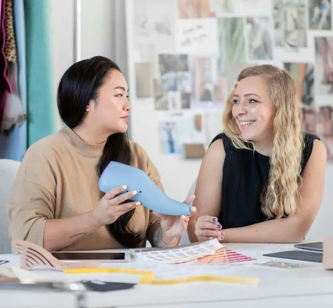 Two ladies sitting at a desk learning how to be a shoe designer.