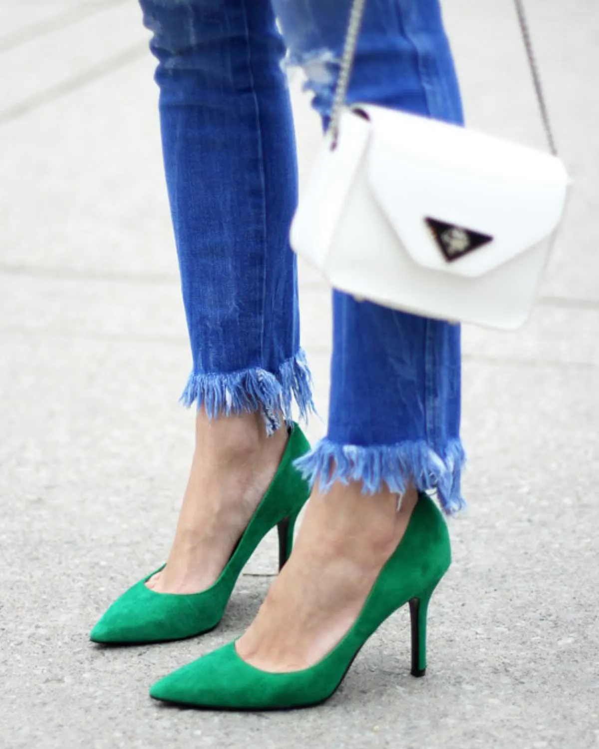 Close up image of women wearing jeans with a pair of green heels on grey background.