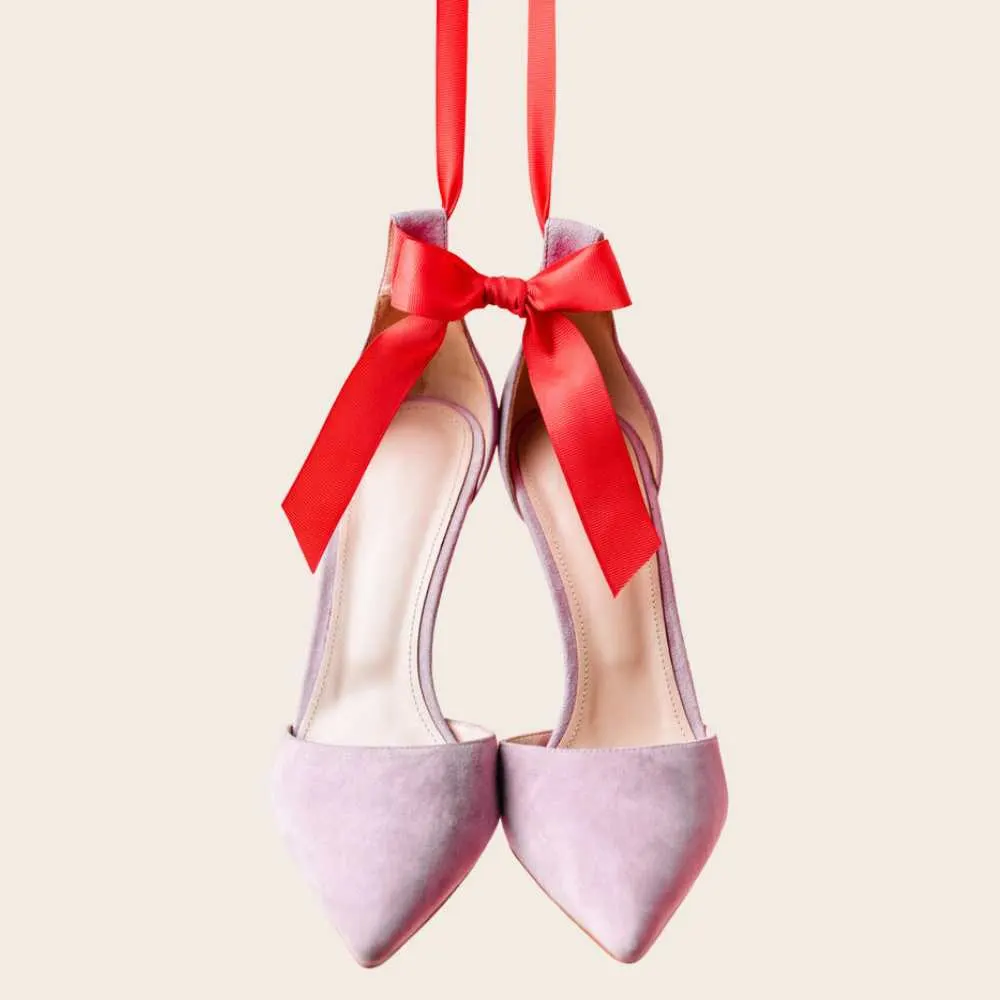 Pair of lavender suede heels hanging from a large red ribbon.
