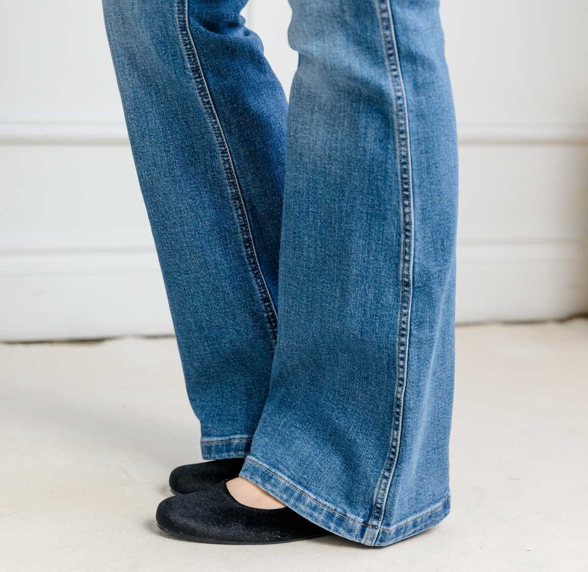 Close of up woman's legs wearing long blue flared jeans with black ballerina flats.
