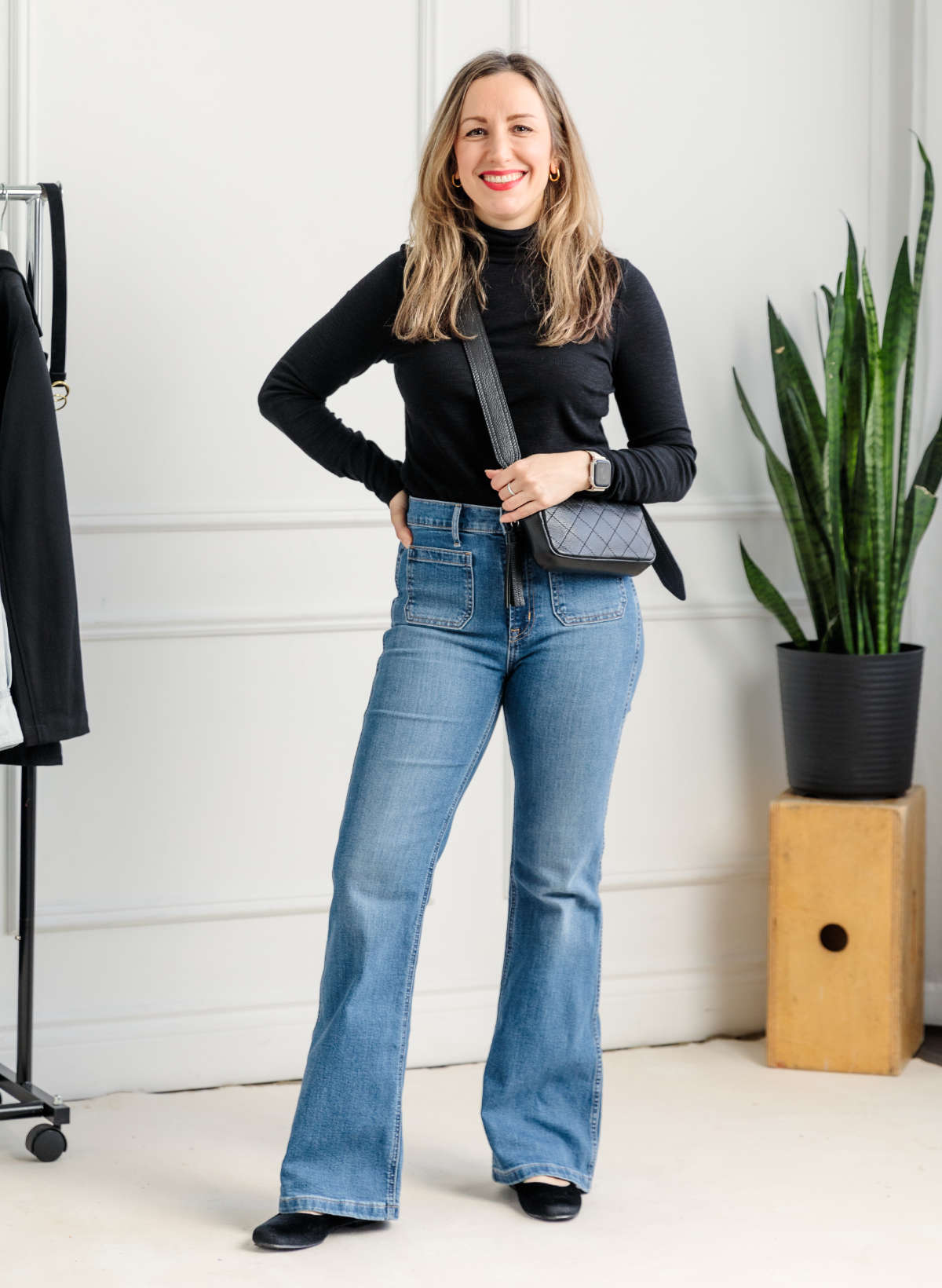 Woman wearing full length flare jeans with Mary Jane flats and black turtleneck.