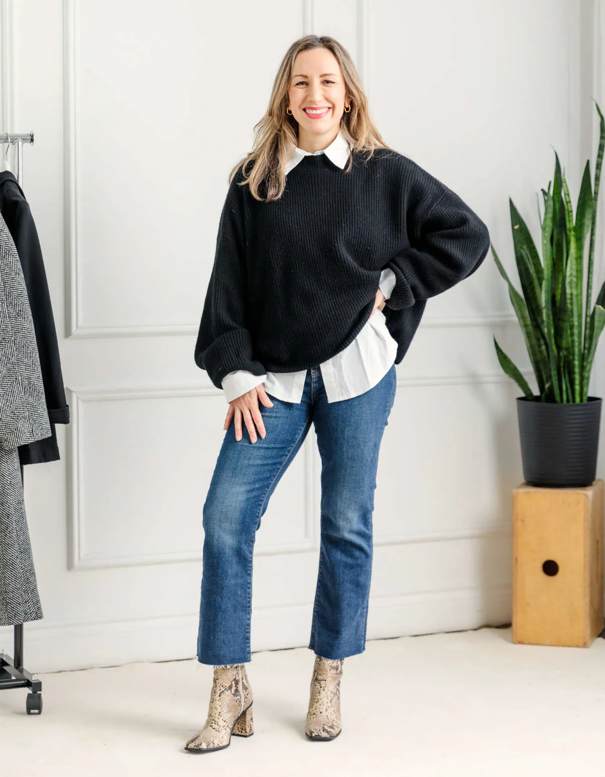 Woman wearing kick flare jeans with ankle boots and black sweater over a white shirt.