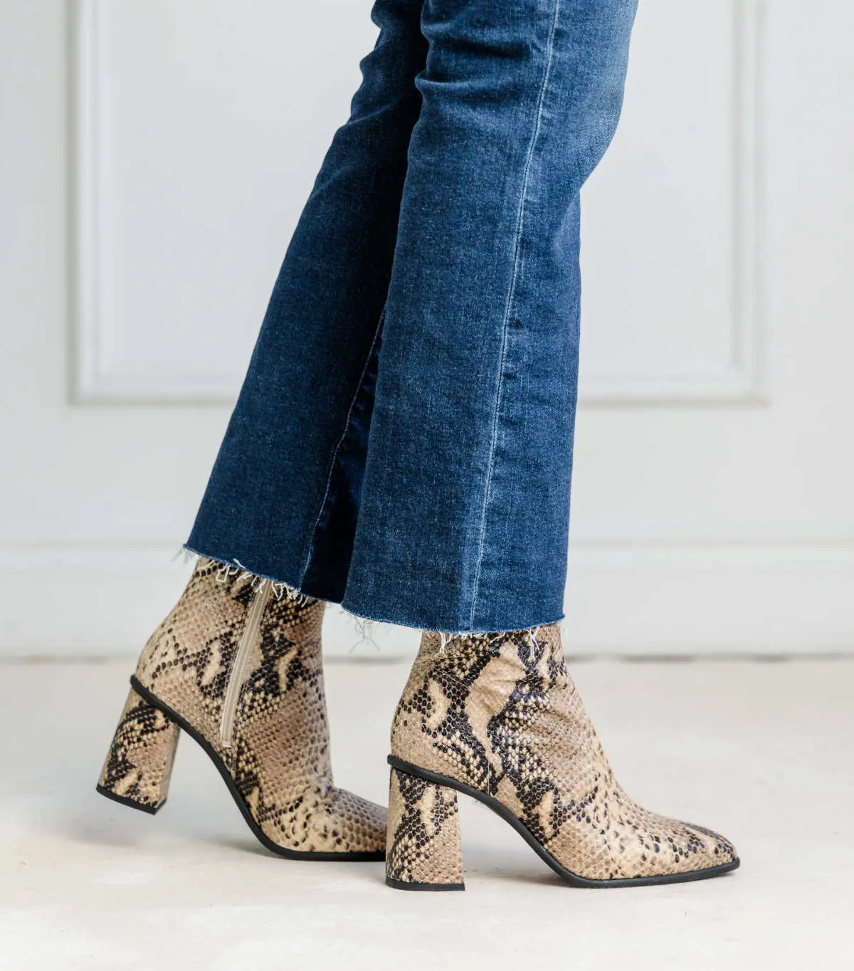 Close of up woman wearing blue cropped flared jeans with snake print ankle boots with block heel.